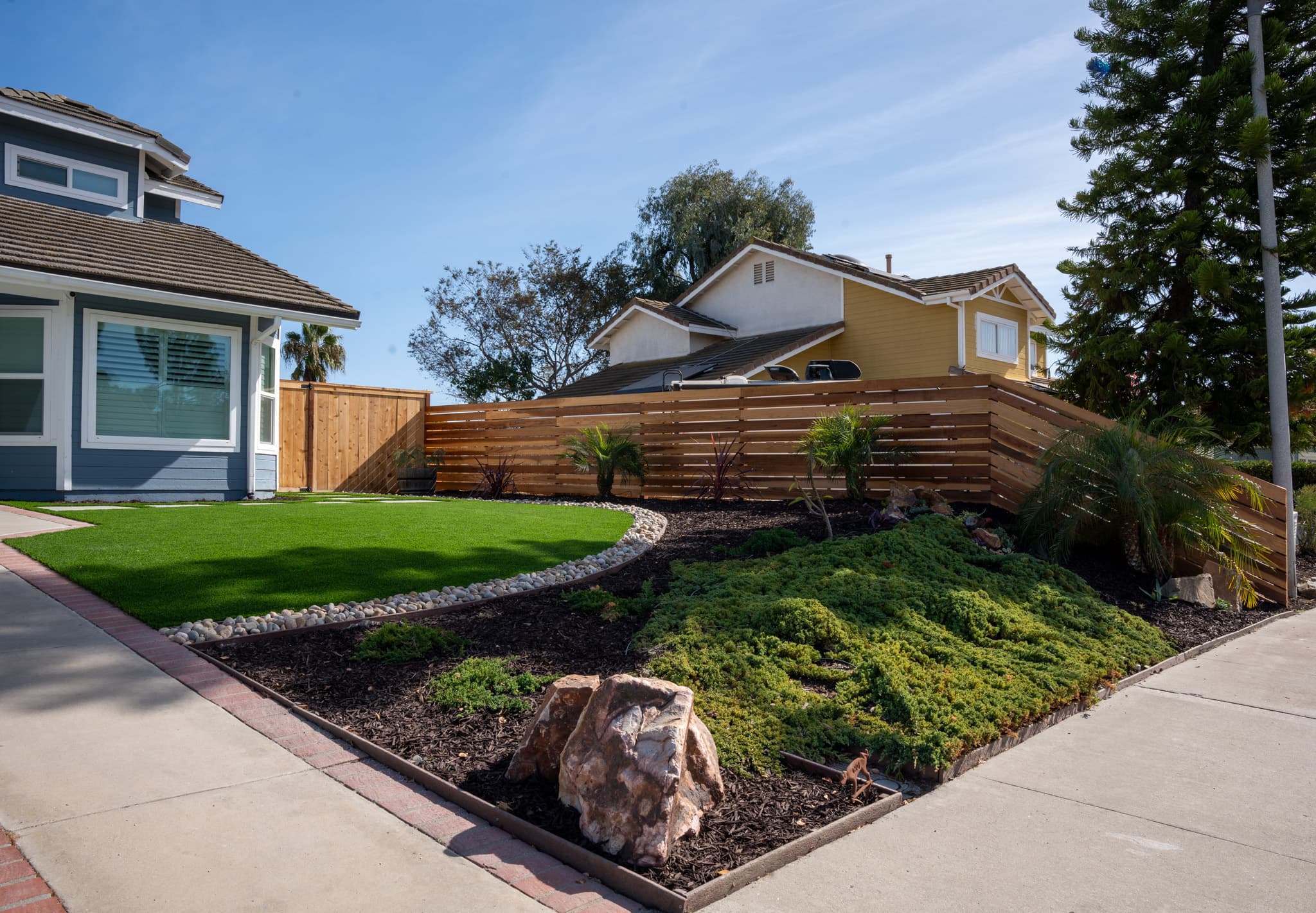 Modern front yard with artificial turf, custom wooden fence, and landscaped garden in San Diego.