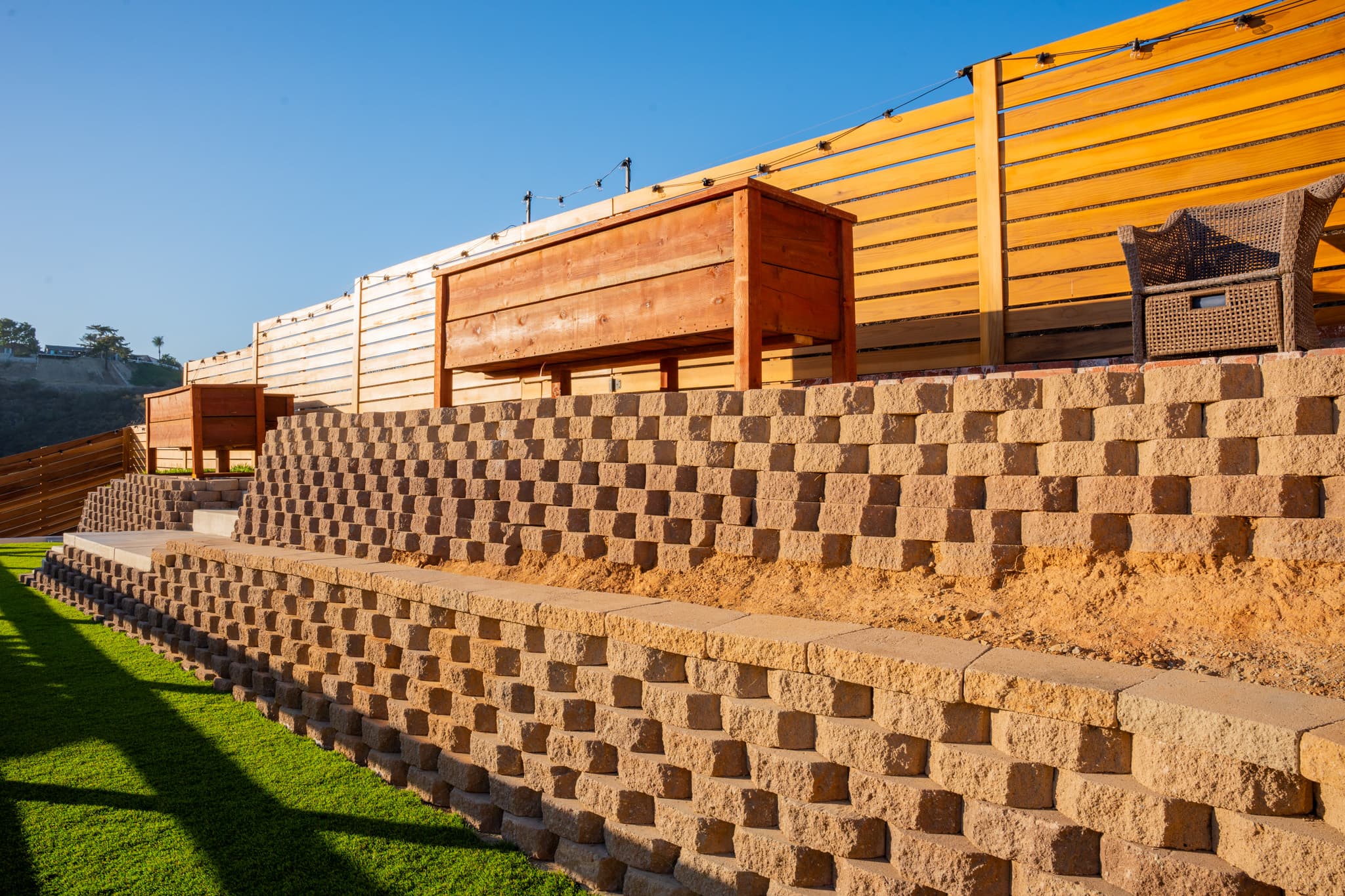 A terraced backyard featuring brick and concrete retaining walls, raised garden planters, and a modern wooden fence in San Diego.